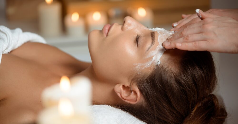 A woman receiving a facial treatment in a relaxing spa setting with candles in the background