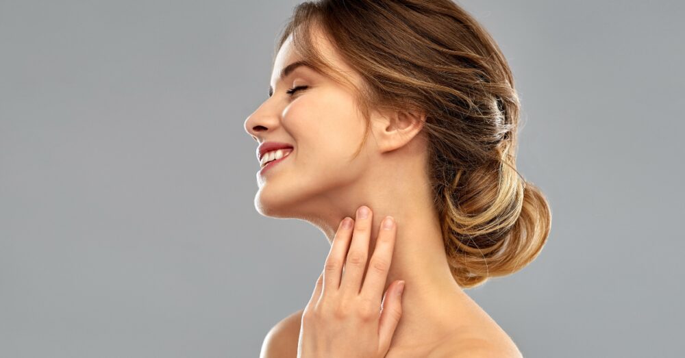 Woman smiling with her head tilted back, lightly touching her neck