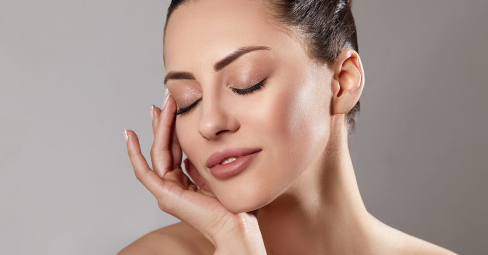Woman lightly touching the side of her face against a neutral background
