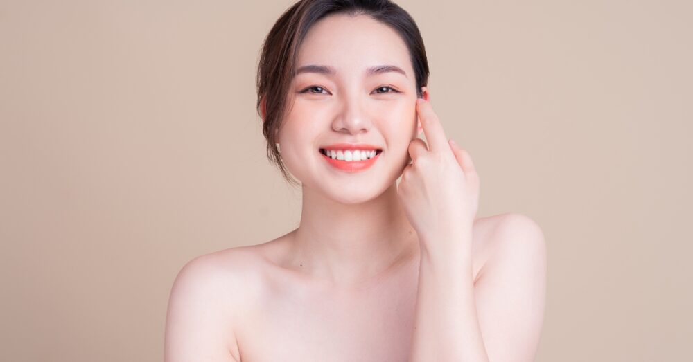 Woman with clear skin smiling at the camera against a beige background